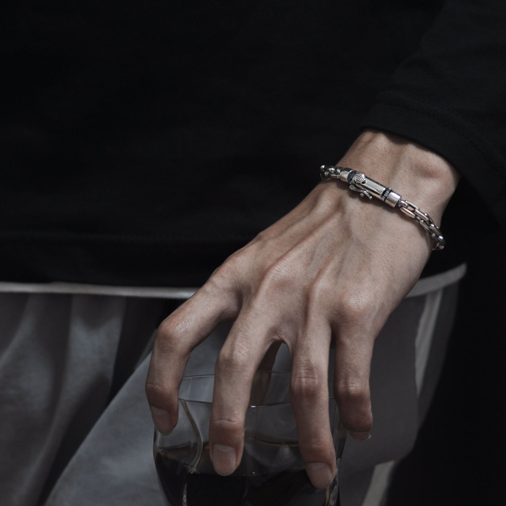 Hand wearing a bracelet holding a glass of red wine against a dark background
