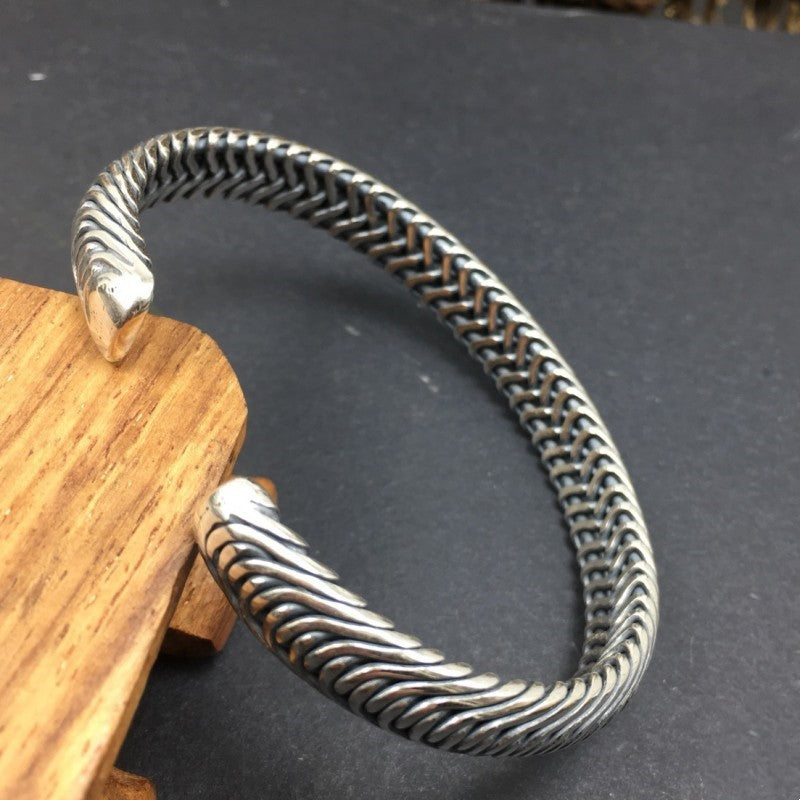 An overhead angled shot of the Nordic Frost Silver Cuff draped elegantly over a polished wood block. The unique perspective clearly shows the hollow-free, highly structured interior weave pattern, proving its dense, solid 925 sterling silver craftsmanship.