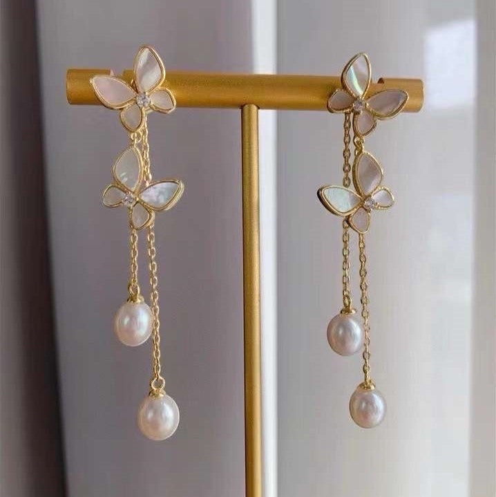 BoxUnboxed gold-plated brass butterfly tassel earrings with freshwater pearls and iridescent shell wings.