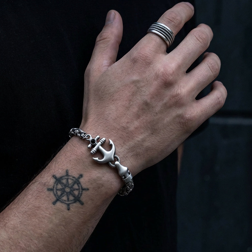 Hand wearing a silver bracelet with an anchor design on a dark background